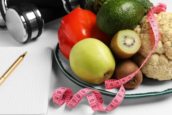 Healthy diet. Plate with products, measuring tape and notebook on white wooden table, closeup