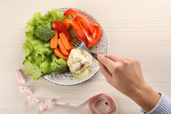 Healthy diet. Woman eating fresh vegetables at light wooden table, top view