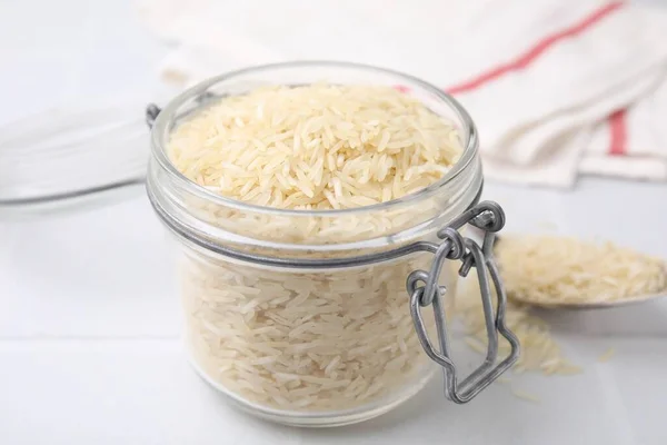 Raw rice in glass jar on white table, closeup