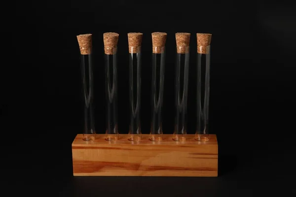 Test tubes in wooden stand on black background. Laboratory glassware