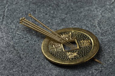 Akupunktur iğneleri ve gri desenli masa üzerindeki antik madeni para, yakın plan.