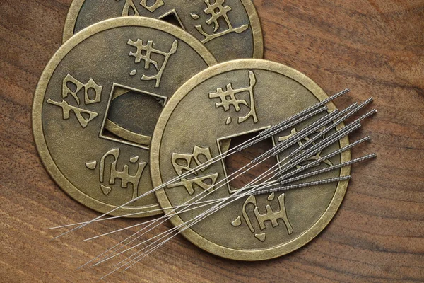 Acupuncture needles and ancient coins on wooden table, flat lay