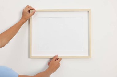 Genç adam beyaz duvarlara resim çerçevesi asıyor.