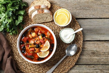 Meat solyanka soup with sausages, olives and vegetables served on wooden table, flat lay. Space for text clipart