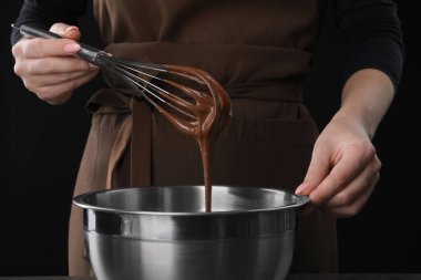 Çikolatalı kremayı siyah arka planda karıştıran çırpmalı kadın, yakın plan.