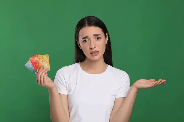 Confused woman with credit cards on green background. Debt problem