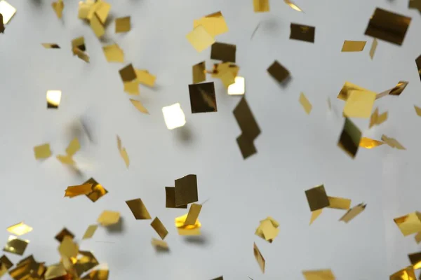 Shiny golden confetti falling down on light grey background
