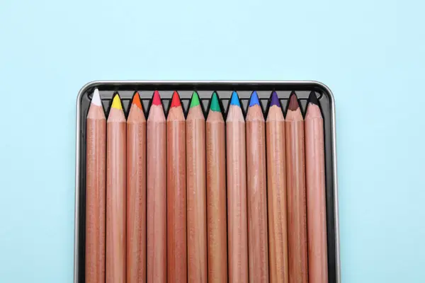 Colorful pastel pencils in box on light blue background, top view. Drawing supplies