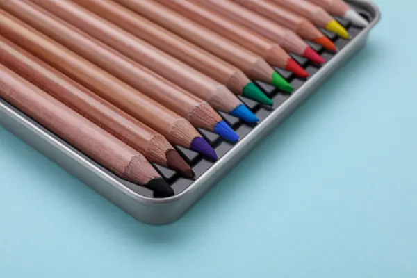 Colorful pastel pencils in box on light blue background, closeup. Drawing supplies