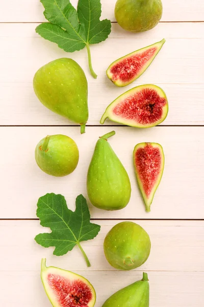Cut and whole green figs with leaves on white wooden table, flat lay