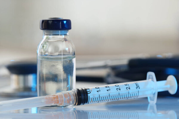 Glass vial, syringe and stethoscope on white table, closeup