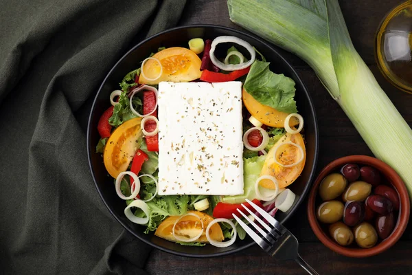 Bowl of tasty salad with leek, cheese and olives served on wooden table, flat lay
