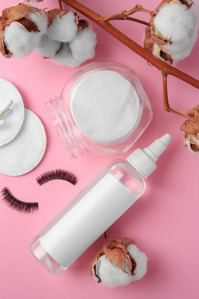 Bottle of makeup remover, cotton flowers, pads and false eyelashes on pink background, flat lay