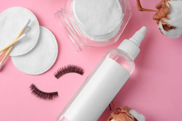 Bottle of makeup remover, cotton flowers, pads, swabs and false eyelashes on pink background, flat lay