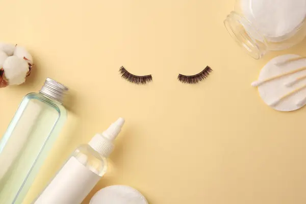 Flat lay composition with bottles of makeup removers and false eyelashes on yellow background