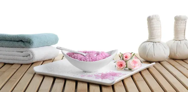 Bowl of pink sea salt, beautiful roses, herbal bags and towels on wooden table against white background