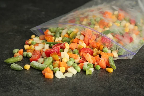 Zip bag with different frozen vegetables on grey table, closeup