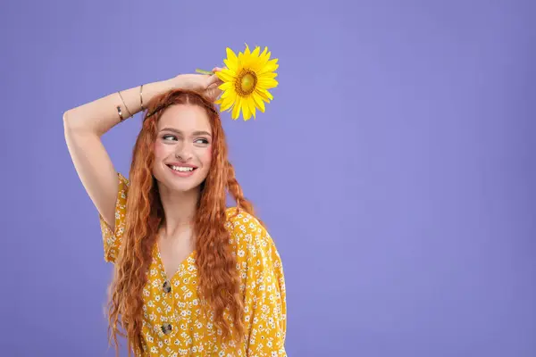 Beautiful young hippie woman with sunflower on violet background, space for text
