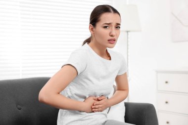Evdeki kanepede karın ağrısı çeken bir kadın. Sağlıksız mide.
