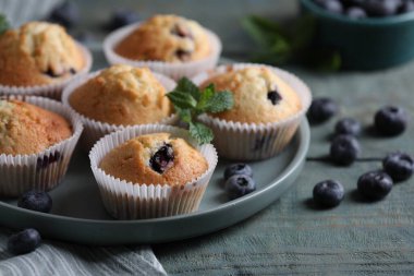 Yaban mersinli lezzetli çörekler ve açık mavi ahşap masada nane şekeri, yakın plan.