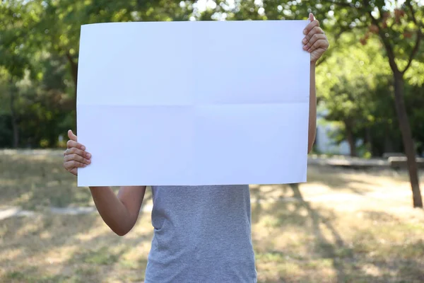 Woman holding blank poster outdoors. Mockup for design