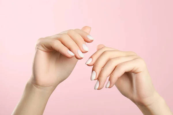 Woman with white polish on nails against pink background, closeup