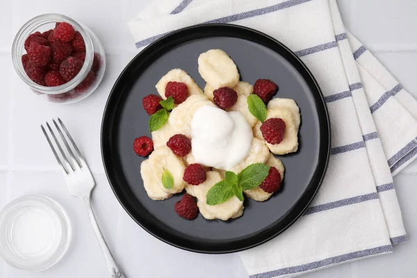Plate of tasty lazy dumplings with raspberries, sour cream and mint leaves on white tiled table, flat lay