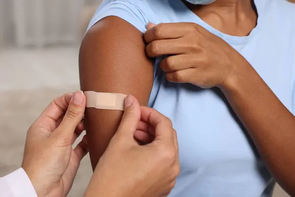 Stock image Doctor putting adhesive bandage on young woman's arm after vaccination indoors, closeup