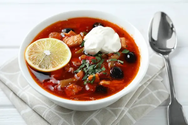 stock image Meat solyanka soup with sausages, olives, vegetables and spoon on white wooden table, closeup