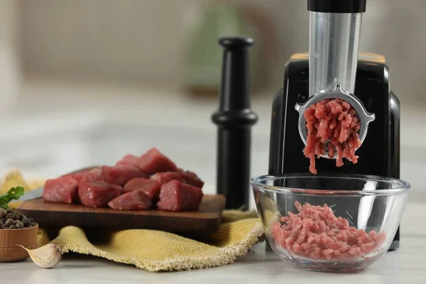 Electric meat grinder with beef mince on white table against blurred background, selective focus. Space for text