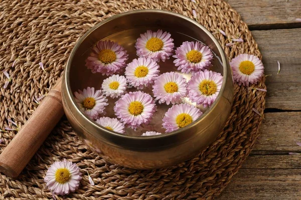 Tibetan singing bowl with water, chrysanthemum flowers and mallet on table