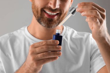 Açık gri arkaplanda kozmetik serumu olan adam, yakın plan.