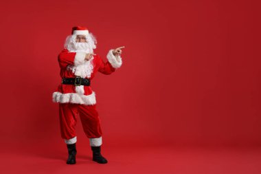 Mutlu noeller. Noel Baba kırmızı arkaplandaki bir şeyi işaret ediyor, metin için boşluk
