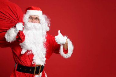 Noel Baba 'nın hediye çantası kırmızı arka planda baş parmağını gösteriyor, mesaj için yer var.