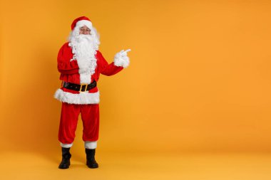 Mutlu noeller. Noel Baba turuncu arkaplandaki bir şeyi işaret ediyor, mesaj için boşluk