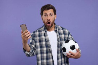 Futbol topu ve mor arka planda akıllı telefonu olan duygusal spor fanatiği.