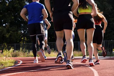 Güneşli bir günde stadyumda koşan bir grup insan