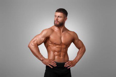 Açık gri arka planda kaslı vücutlu genç bir vücut geliştirici.