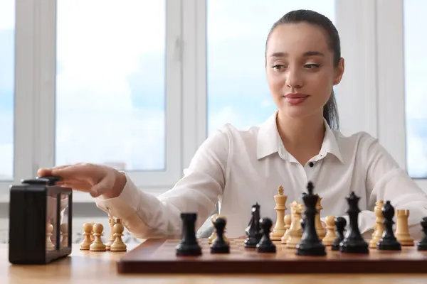 Woman turning on chess clock during tournament at table indoors