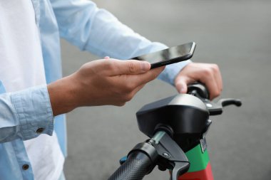 Akıllı telefonu kullanan bir adam açık havada elektrikli scooter 'ın önünü açar ve öder.