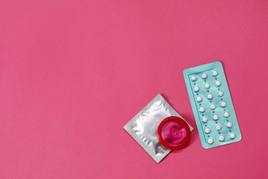 Doğum kontrol tercihi. Eflatun arka planda haplar ve prezervatifler, düz yatak. Metin için boşluk