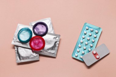 Pembe arka planda doğum kontrol hapları ve prezervatifler. Doğum kontrol yöntemi seçiliyor.