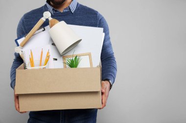 Açık gri arka planda kişisel ofis eşyalarıyla dolu bir kutuya sahip işsiz adam, yakın plan. Metin için boşluk