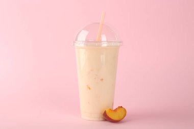 Plastik bardak lezzetli smoothie ve pembe arka planda taze şeftali.
