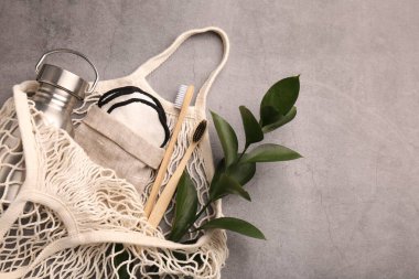 Farklı nesnelerin olduğu balık ağı çantası ve gri masa üzerinde yeşil dal, üst görüş ve metin için boşluk. Bilinçli tüketim