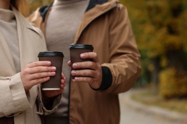 Sonbahar parkında kahve fincanlarıyla vakit geçiren mutlu genç çift, yakın çekim. Metin için boşluk