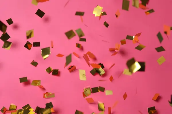 Shiny golden confetti falling down on pink background