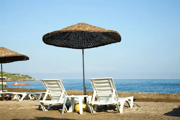 Two lounge chairs and beach umbrella on sea shore