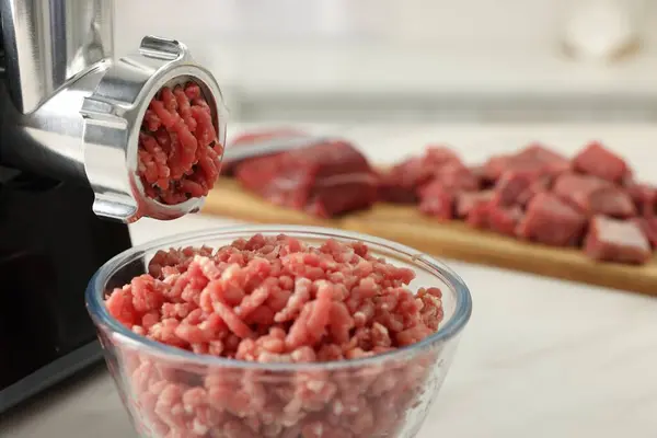 Electric meat grinder with minced beef on white table, closeup