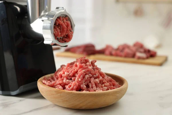 Electric meat grinder with minced beef on white marble table indoors, space for text